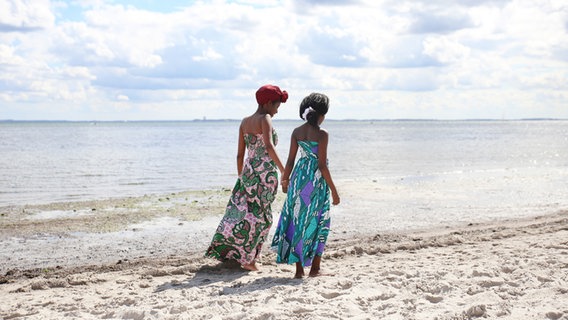 Zwei Frauen mit langen Kleidern gehen einen Strand entlang. © time. / photocase.de Foto: time. / photocase.de