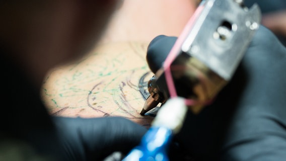 Ein Tätowierer sticht jemandem ein Tattoo. © picture alliance/Christophe Gateau/dpa Foto: Christophe Gateau