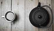 Ein schwarzer Teekessel neben einem Becher mit Tee. © andrey-fo / photocase.de Foto: andrey-fo / photocase.de