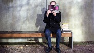 Lesender Mann auf einer Parkbank. © NDR / Friederike Göckeler Foto: Friederike Göckeler