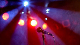 Ein Mikrofon auf einem Ständer, im Hintergrund rote und blaue Bühnenbeleuchtung. © Picture Alliance Foto: Britta Pedersen
