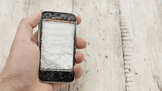 Eine Hand hält ein Smartphone mit gesplittertem Bildschirm. © imago/Westend61 