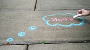 Ein Mann malt mit Kreide eine Sprechblase mit dem Wort "Hallo" auf den Boden. © N-JOY Foto: Eva Köhler
