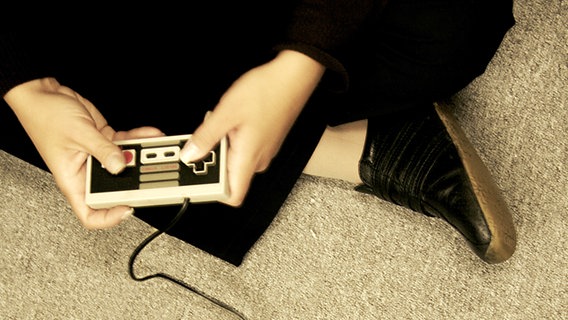 Eine Person sitzt im Schneidersitz und hat einen Nintendo Conrtoller in der Hand. © la dina / photocase.de Foto: la dina