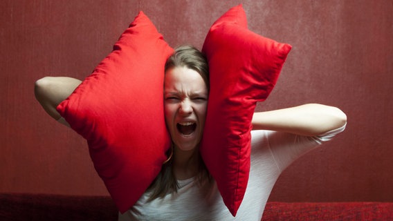 Frau schreit und hält sich zwei rote Kissen gegen die Ohren © picture alliance/chromorange Foto: CHROMORANGE / Bernd Juergens