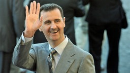 Bassar al-Assad hebt grüßend die Hand  