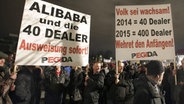 Pegida-Demonstranten halten ein Plakat hoch mit der Aufschrift: "Alibaba und die 40 Dealer. Ausweisung sofort!" © epd-bild Foto: Matthias Schumann