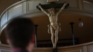 Jesus am Kreuz in Kirche. Im Vordergrund der Hinterkopf eines Mannes. © NDR 