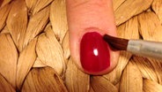 Ein Pinsel mit Nagellackentferner korrigiert einen Finger mit rotem Nagellack. © NDR 