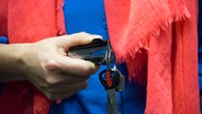 Eine Hand hält einen Schlüsselring und einen Tackernadel-Entferner. © NDR 