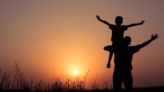 Ein Vater trägt seinen Sohn auf den Schultern im Sonnenuntergang. © photocase / altanaka Foto: altanaka