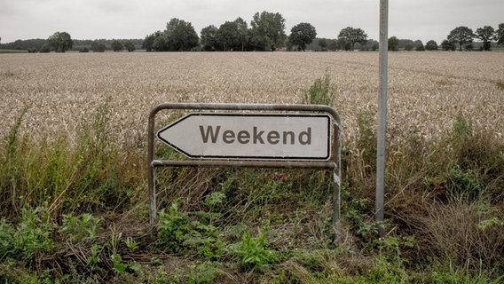 Auf einem Wegweiser am Feld steht in großen Buchstaben Weekend. © Photocase Foto: Jaeschko