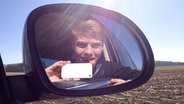 Ein junger Mann schaut in den Außenspiegel eines Autos und macht ein Selfie. © fotolia Foto: grafikplusfoto
